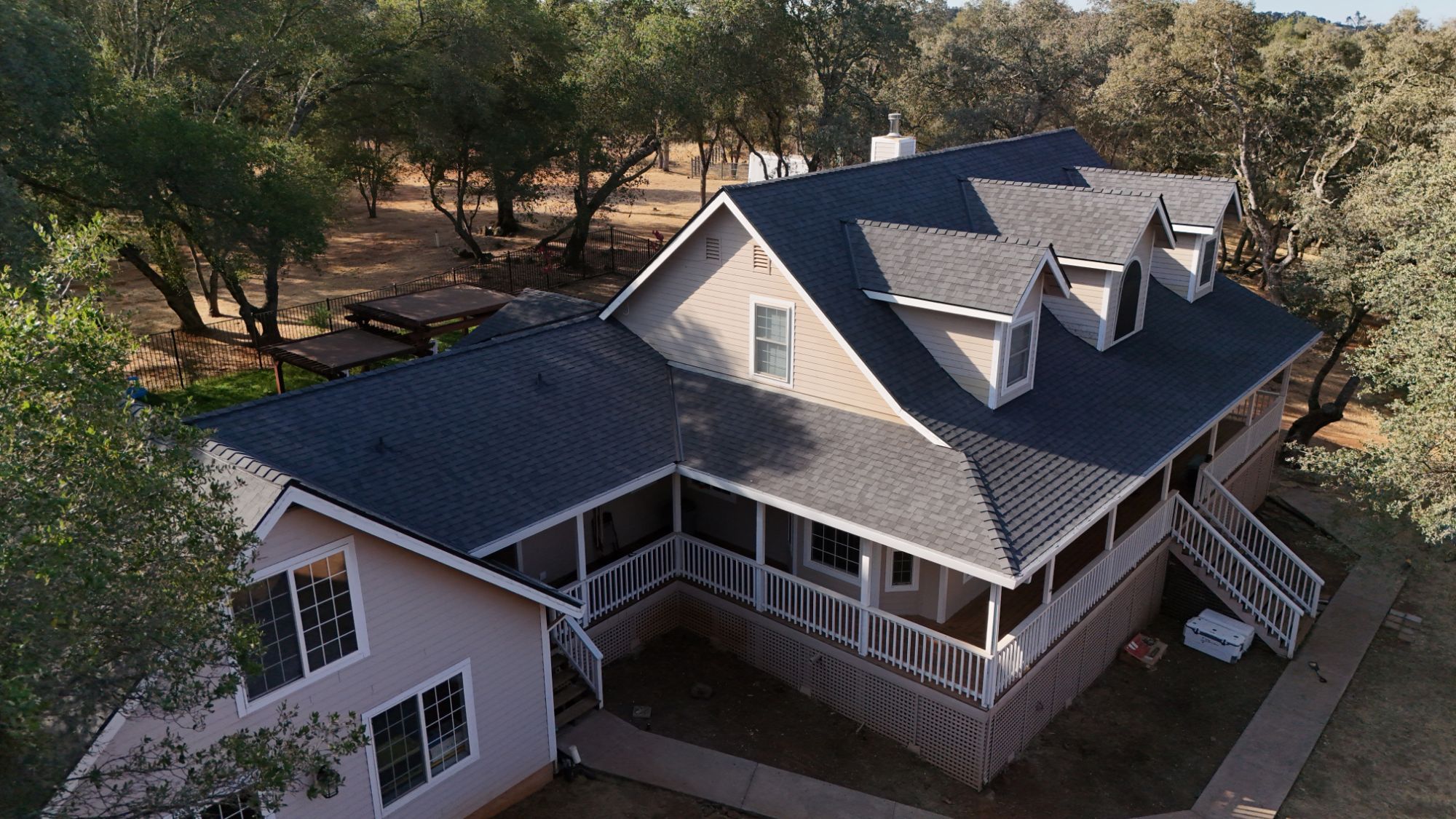 Aerial view of a Cameron Park farmhouse with a new CertainTeed Landmark Solaris roof in Moire Black and a wraparound porch